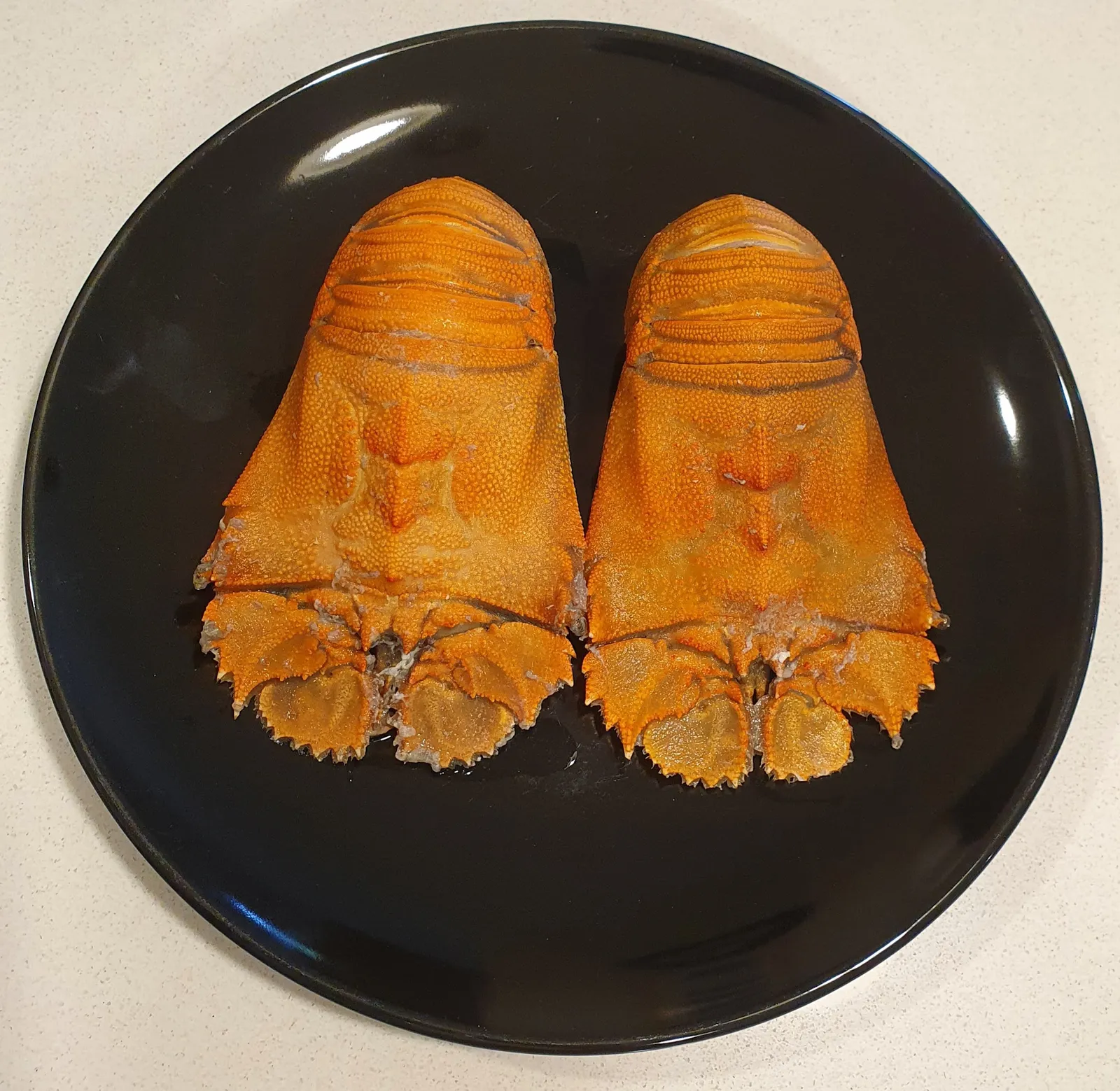 Two cooked Balmain bug halves on a black plate, overhead view