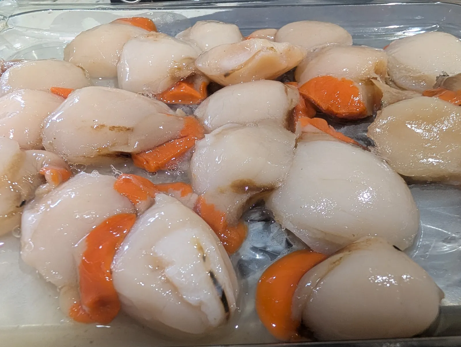 Raw scallop meats with coral/roe in a clear food tray, overhead view